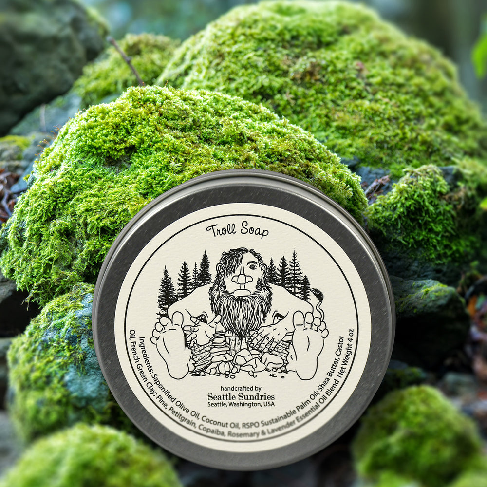 A mossy backdrop showcases a tin of bath soap, featuring a delightful troll illustration, ideal for nourishing your skin.